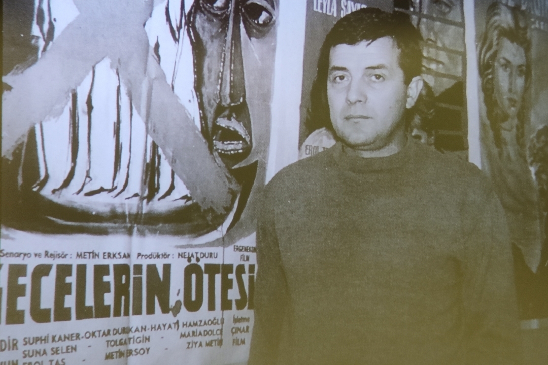 Gecelerin Ötesi filminin posteri önünde Metin Erksan
