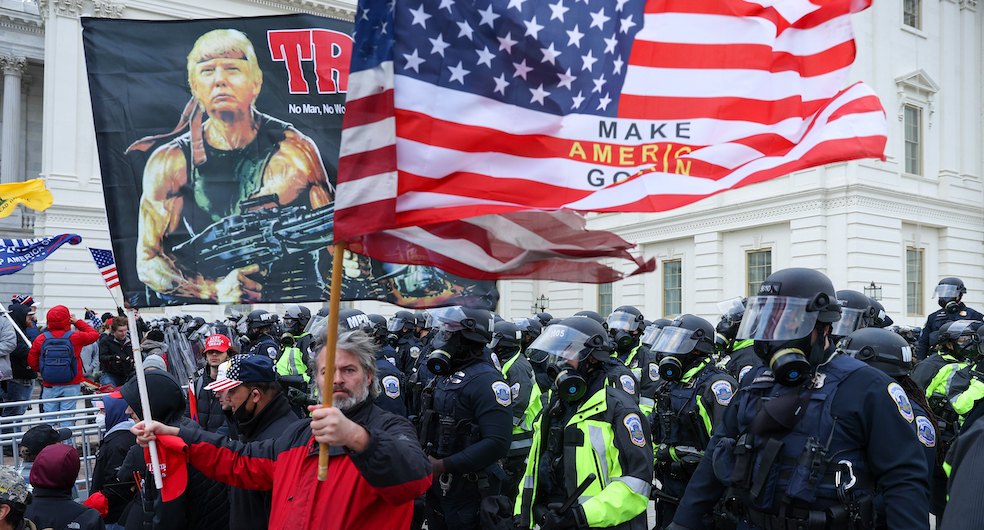 Bir elinde Rambo şeklinde fotomontajlanmış Trump fotoğrafının olduğu, diğer elinde "Make America Great Again" yazılı bayrak taşıyan ABD'li şahıs